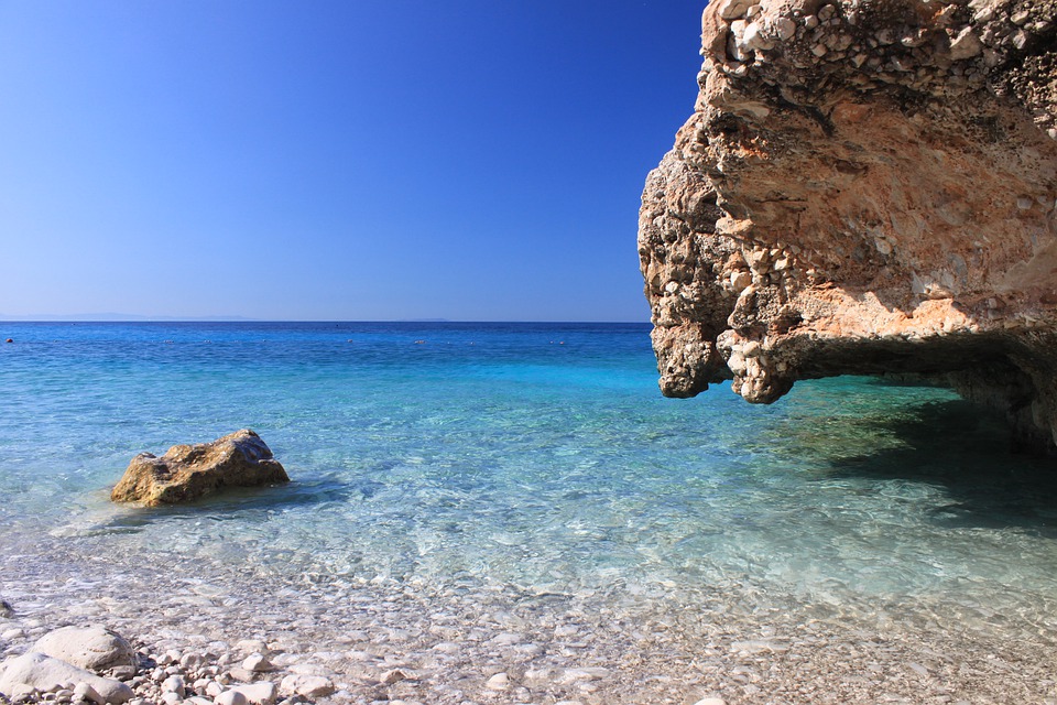 A beach with clear water and a cave in the background is a popular choice for those seeking hot holiday destinations.