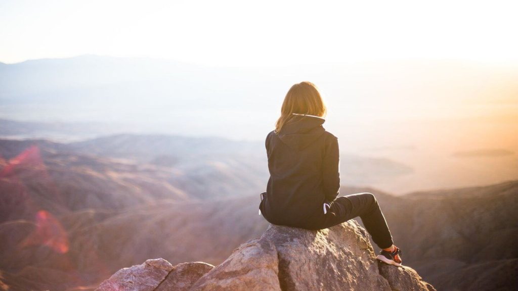 adult sitting on top of a mountain