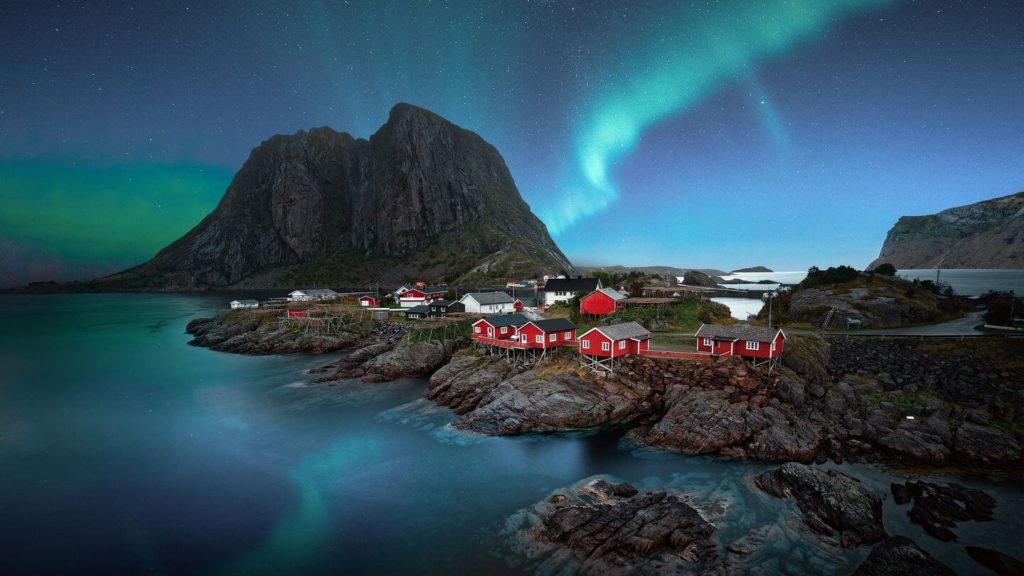 red cottages on rocky shoreline green northern lights Scandinavia