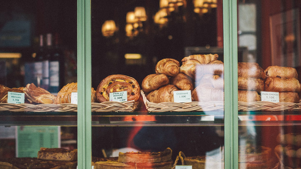 Assorted French pastries, including the historically significant croissant, on display in a bakery shop window with price tags.