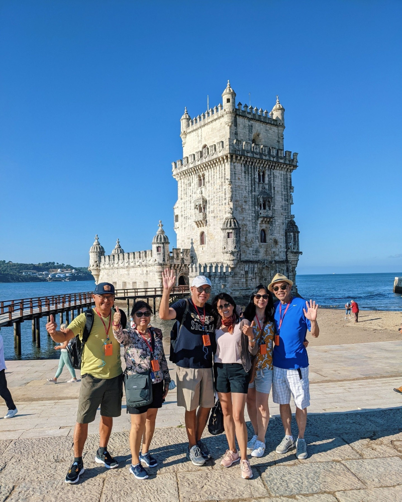 Group of tourists posing with happiness in front of the Belem Tower in Lisbon, Portugal.