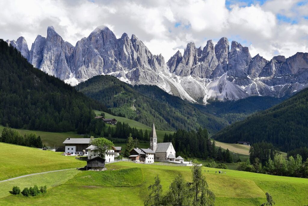 View of green meadows and a small Alpine commune with the jagged Dolomites in the background