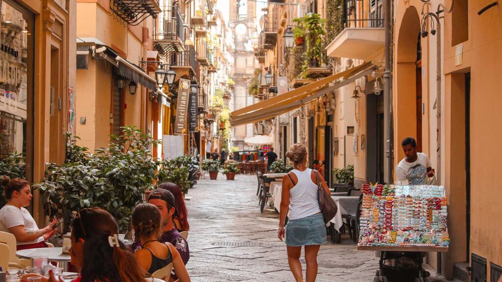 A woman walks up a shaded town-centre street in Sicily