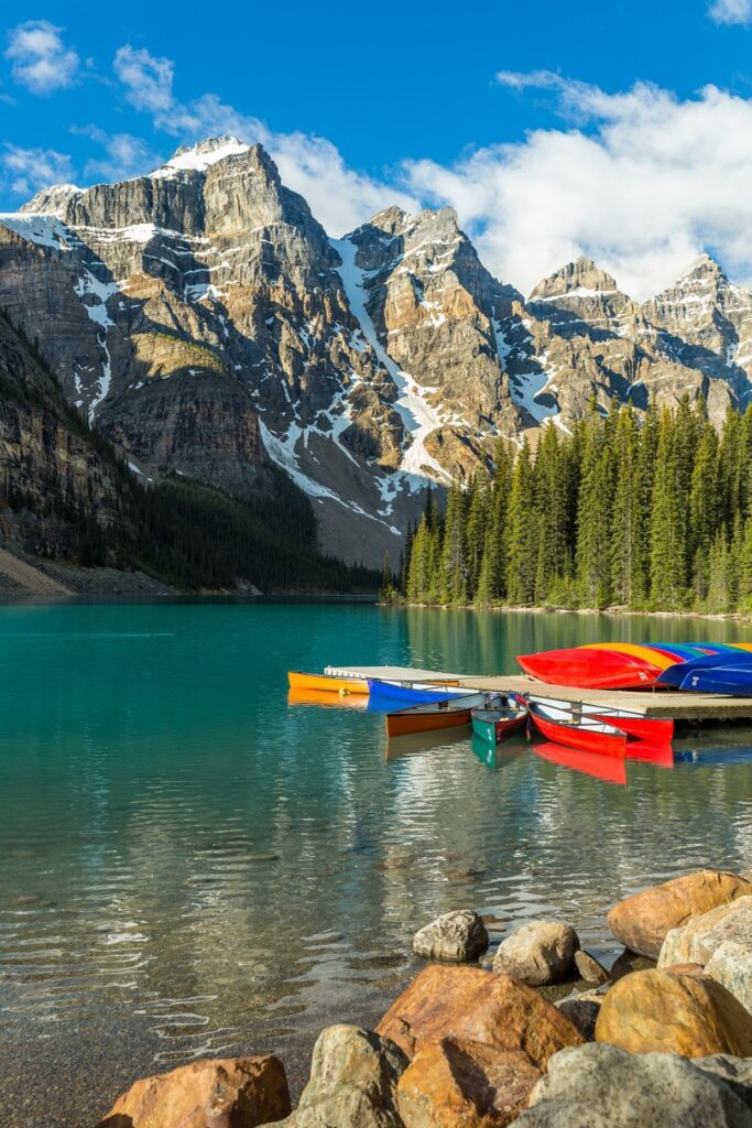 colourful canoes on blue lake surrounded by forest and Canadian Rockies