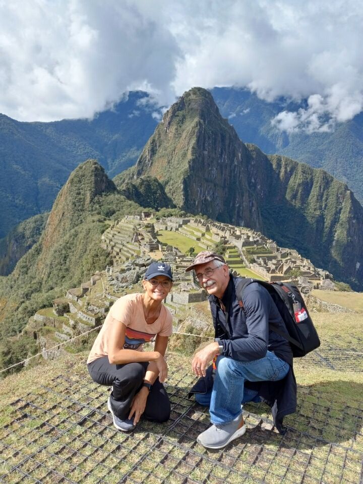 Daughter and father leaning down, posing for photo in front of Machu Picchu on a clear day.