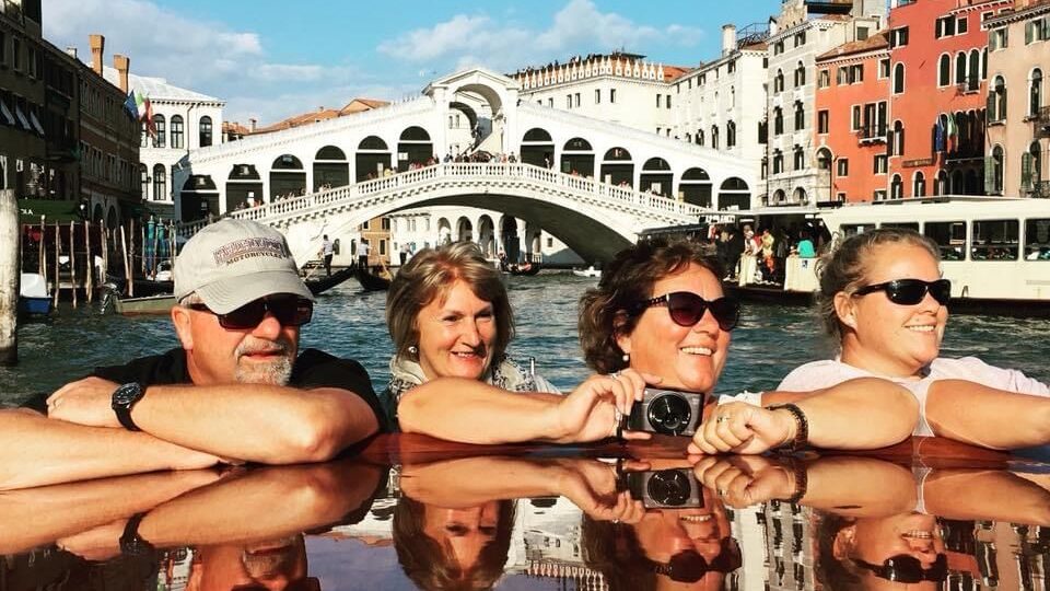 Four people posing for a photo in Venice with river in the background