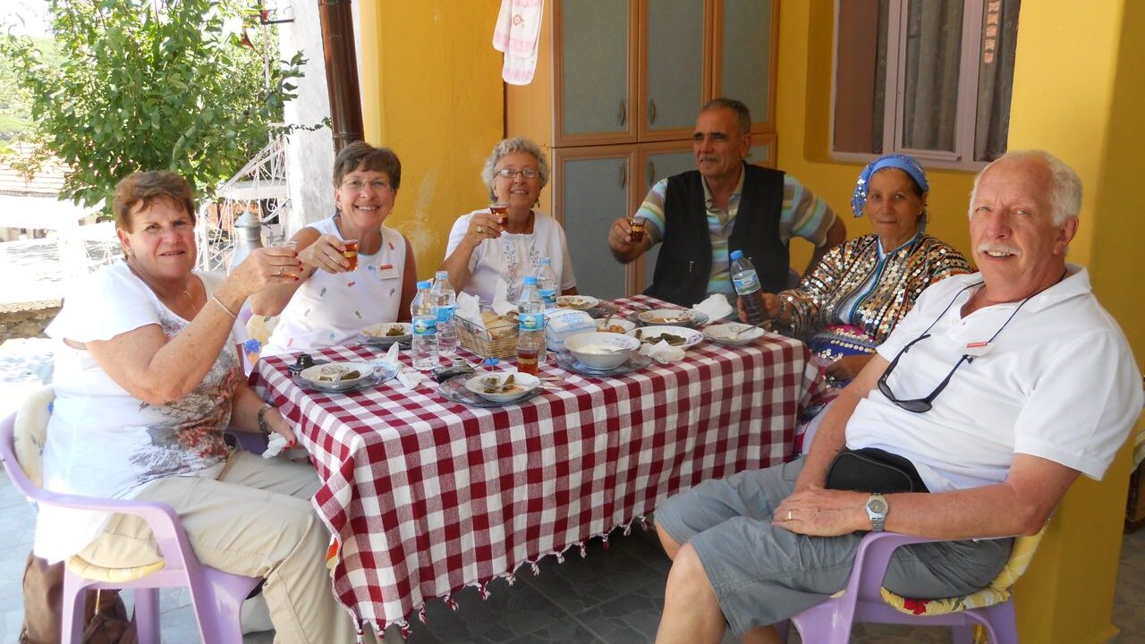 A group of people smile for a photo while at a dining table, holding up small glasses