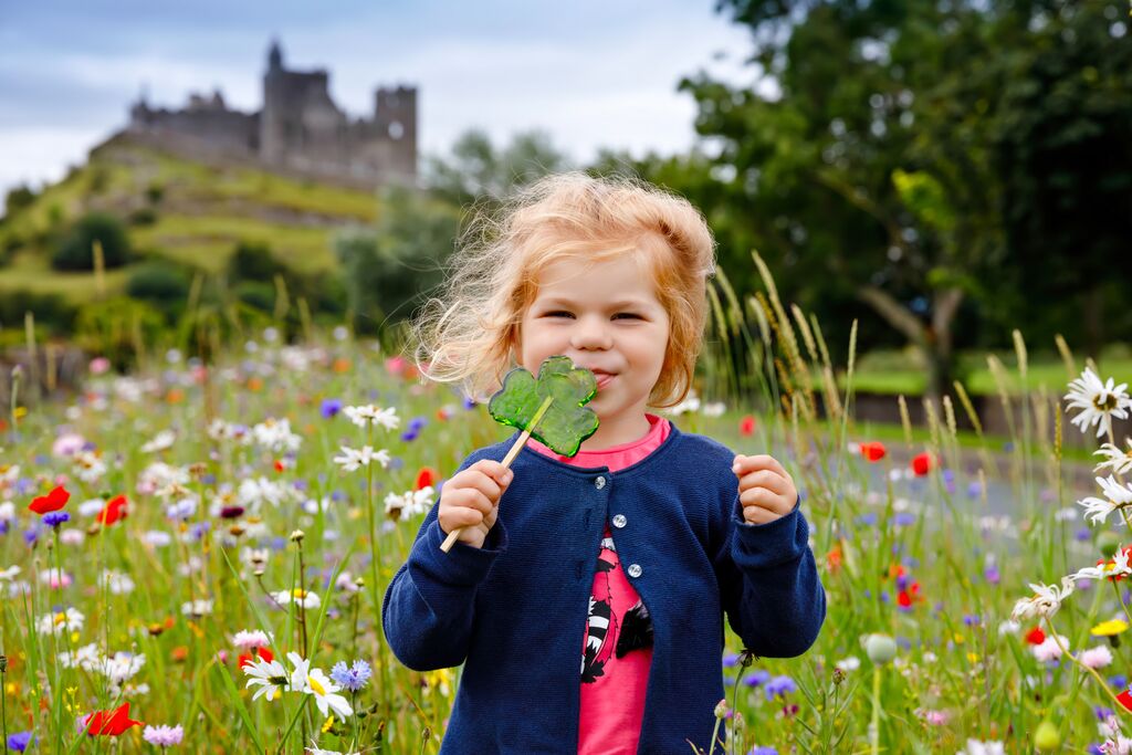 Toddler girl with Irish cloverleaf lollipop playing in meadow