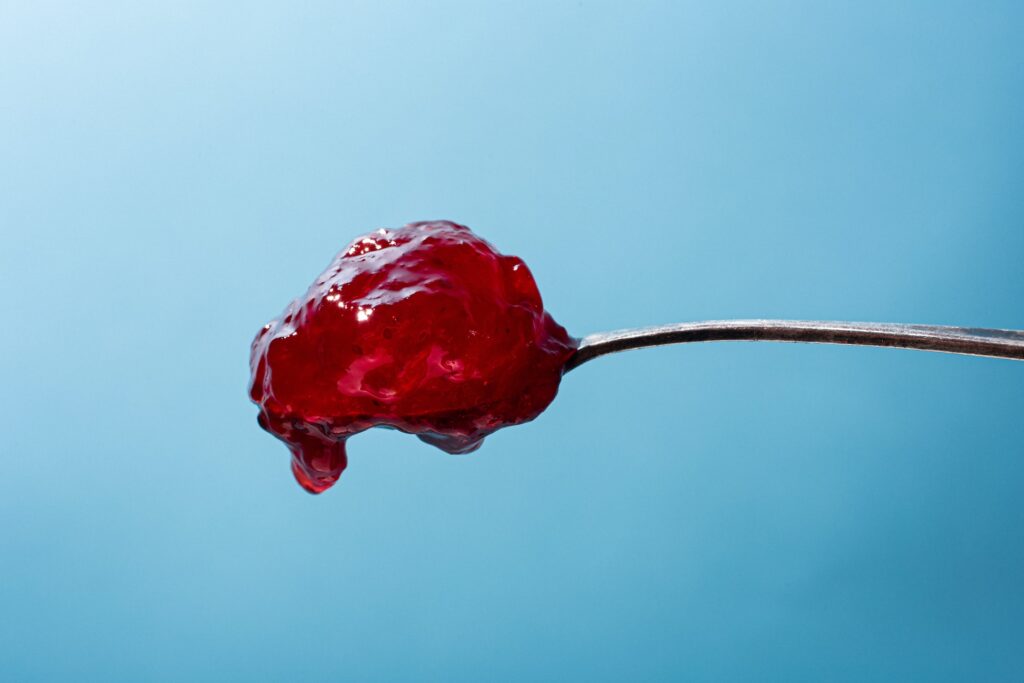 close up of red jam on spoon with blue backdrop