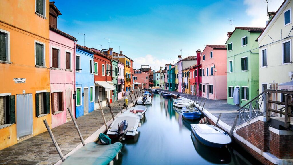 Looking down a canal on Burano Island near Venice at dawn, lined with boats and colorful buildings