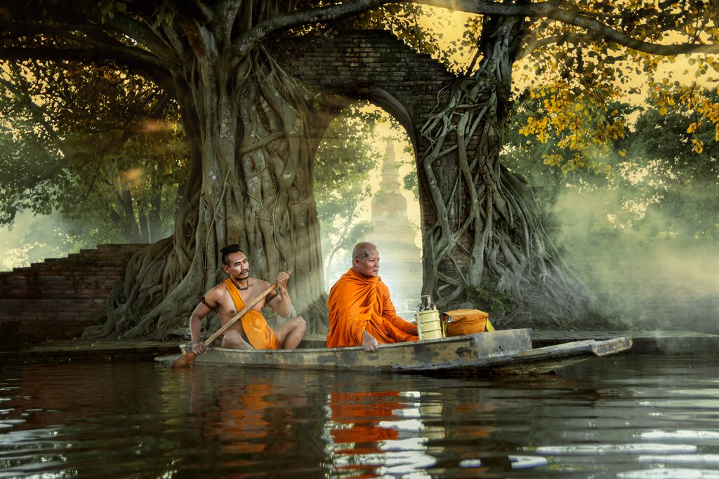 Two monks rowing a boat through water in Thailand.