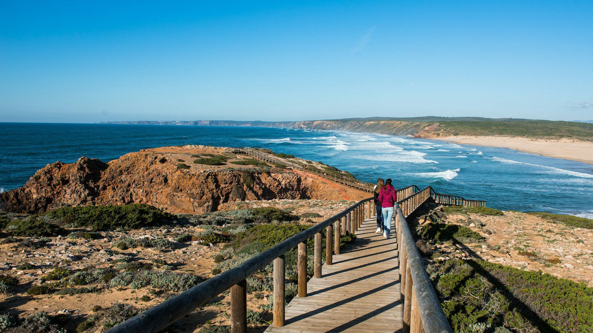 Two female tourists walking down a board walk towards a beach in the Algarve