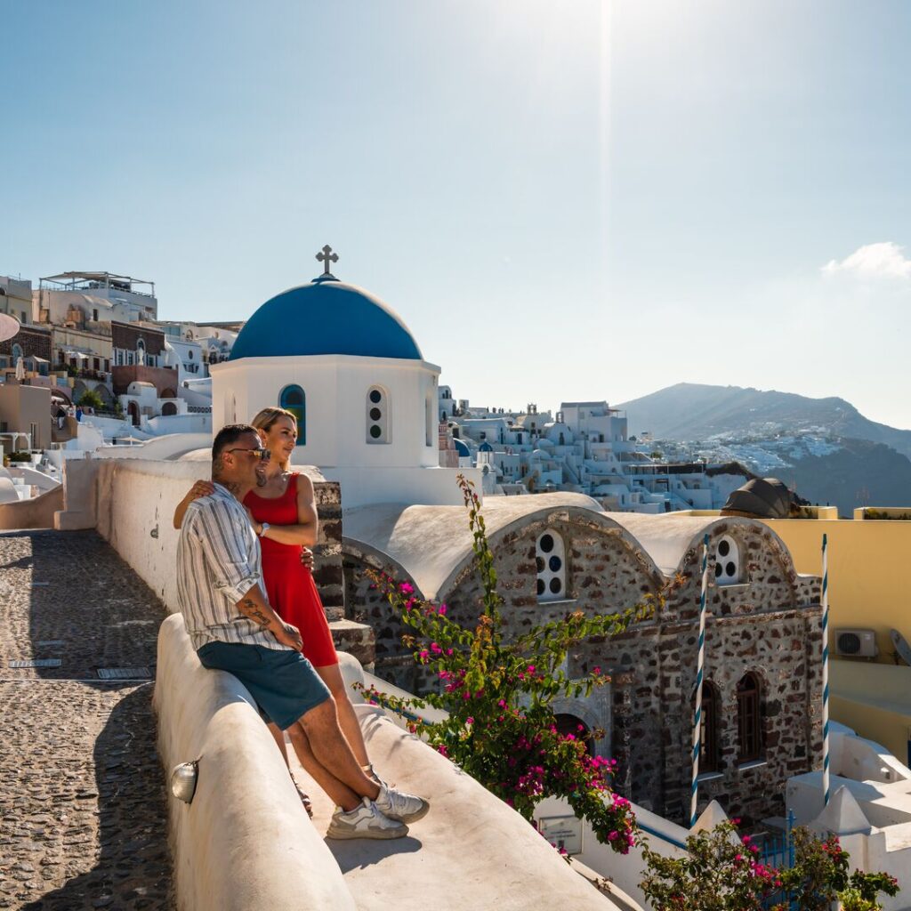 A couple embrace while looking out into the horizon, with Santorini's white-washed houses and blue-domed roofs cascading in the background.