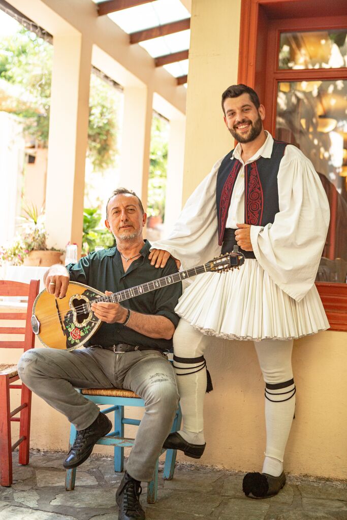 A man with a type of guitar and another in traditional dress pose for a photo.