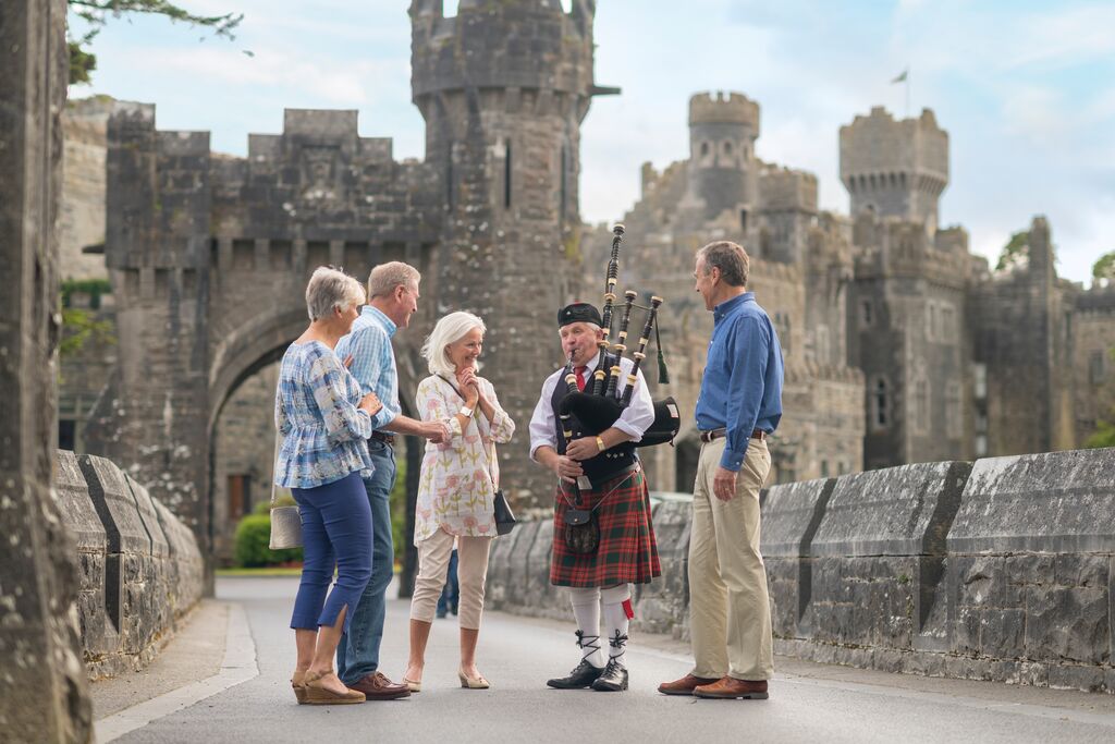 Bagpiper plays to a group of guests in front of a stone castle