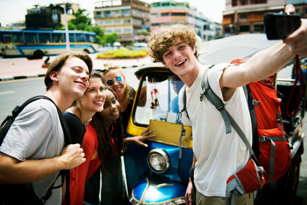 Group of young travelers taking a selfie next to a tuk tuk