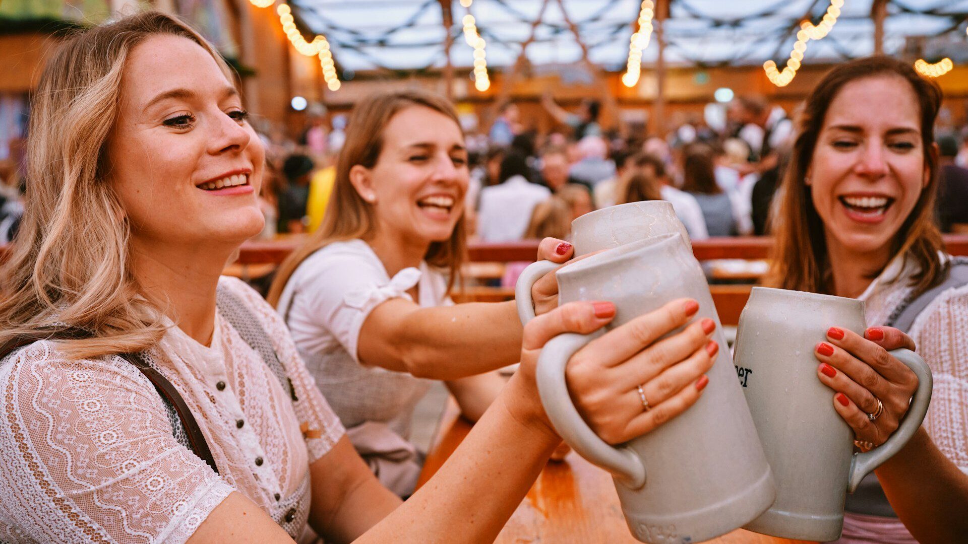 Three women clink large ceramic beer glasses together at Oktoberfest